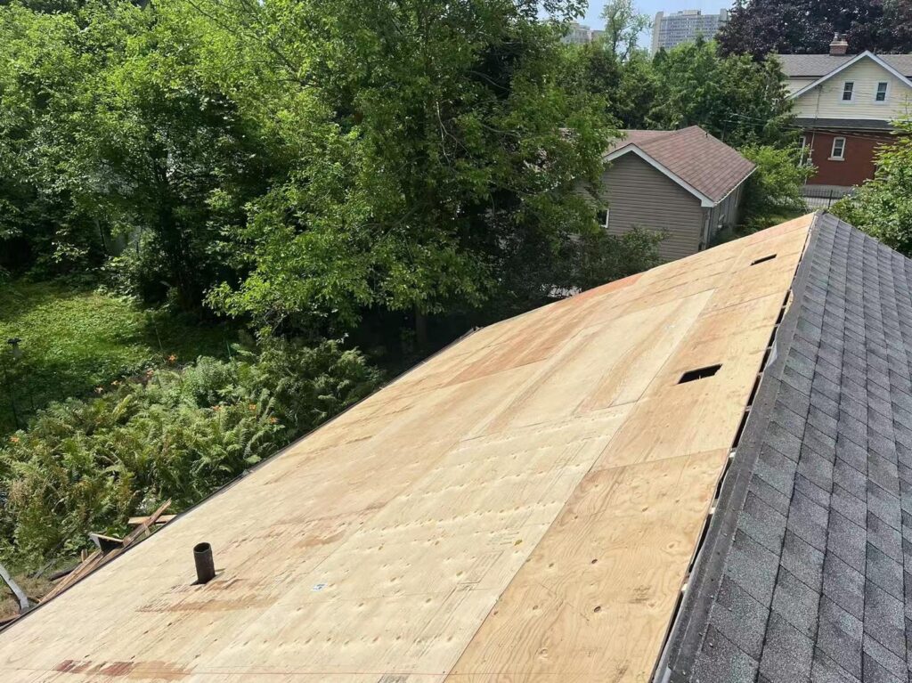 Roof decking exposed beside existing shingles during roofing work